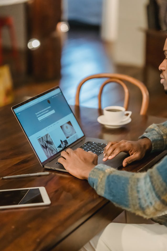 A young adult working on a laptop in a modern, cozy interior with a cup of coffee.